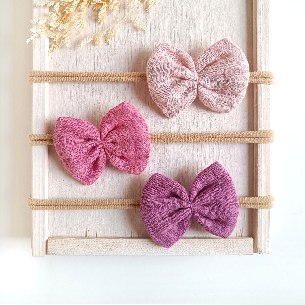 Haarschleifen für Babys aus Musselin in den Farben hellrosa, rosa und lila an einem elastischen Haarband