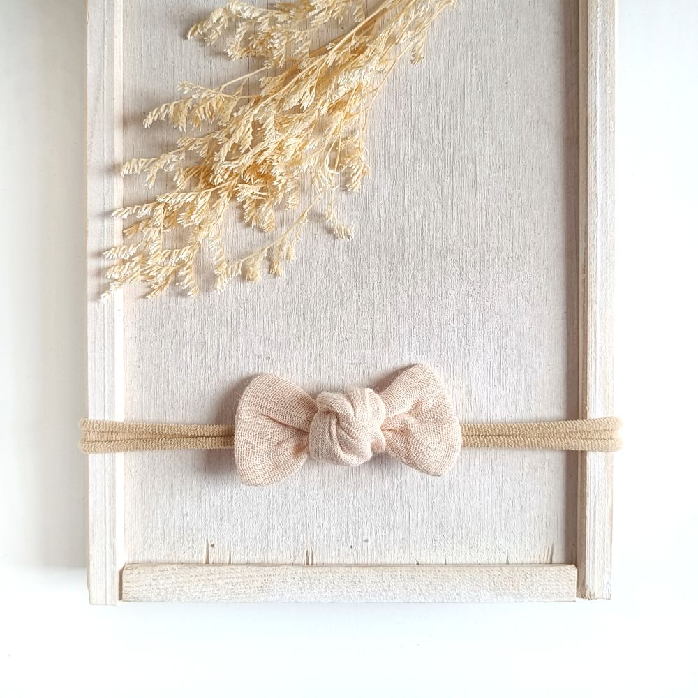 Baby mit kleiner Haarschleife in beige aus Musselin an einem elastischen Haarband