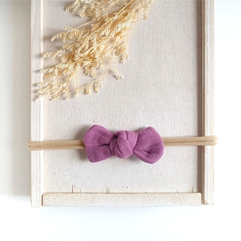 Baby mit kleiner Haarschleife in lila aus Musselin an einem elastischen Haarband