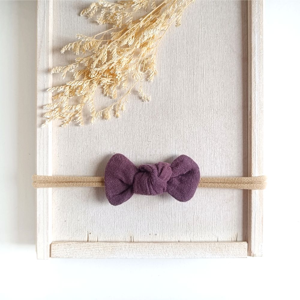 Baby mit kleiner Haarschleife in pflaume aus Musselin an einem elastischen Haarband