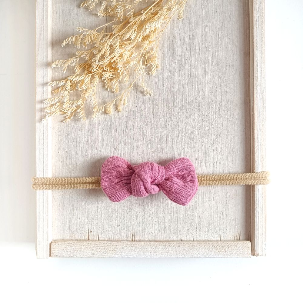 Baby mit kleiner Haarschleife in rosa aus Musselin an einem elastischen Haarband