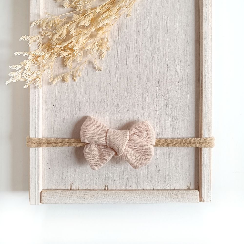 kleine Haarschleife aus Musselin für Babys in beige an einem elastischen Haarband