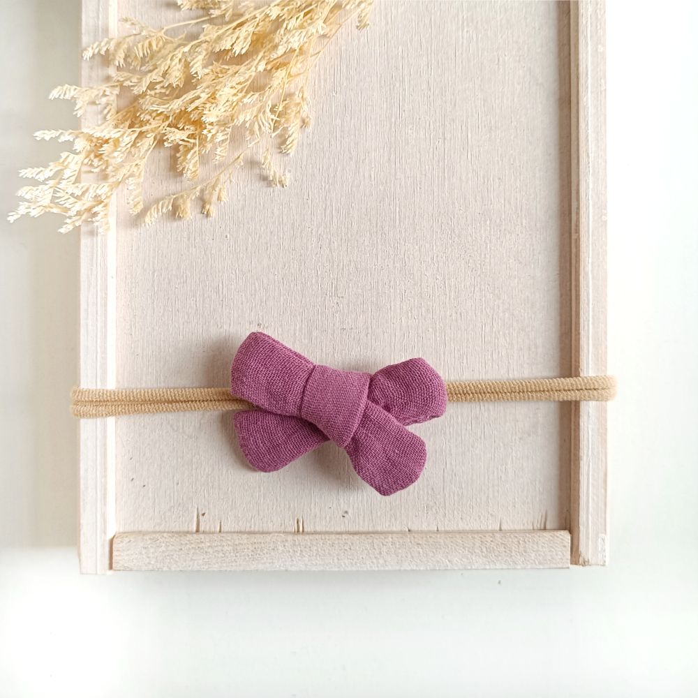 kleine Haarschleife für Babys aus Musslin in lila an einem elastischen Haarband