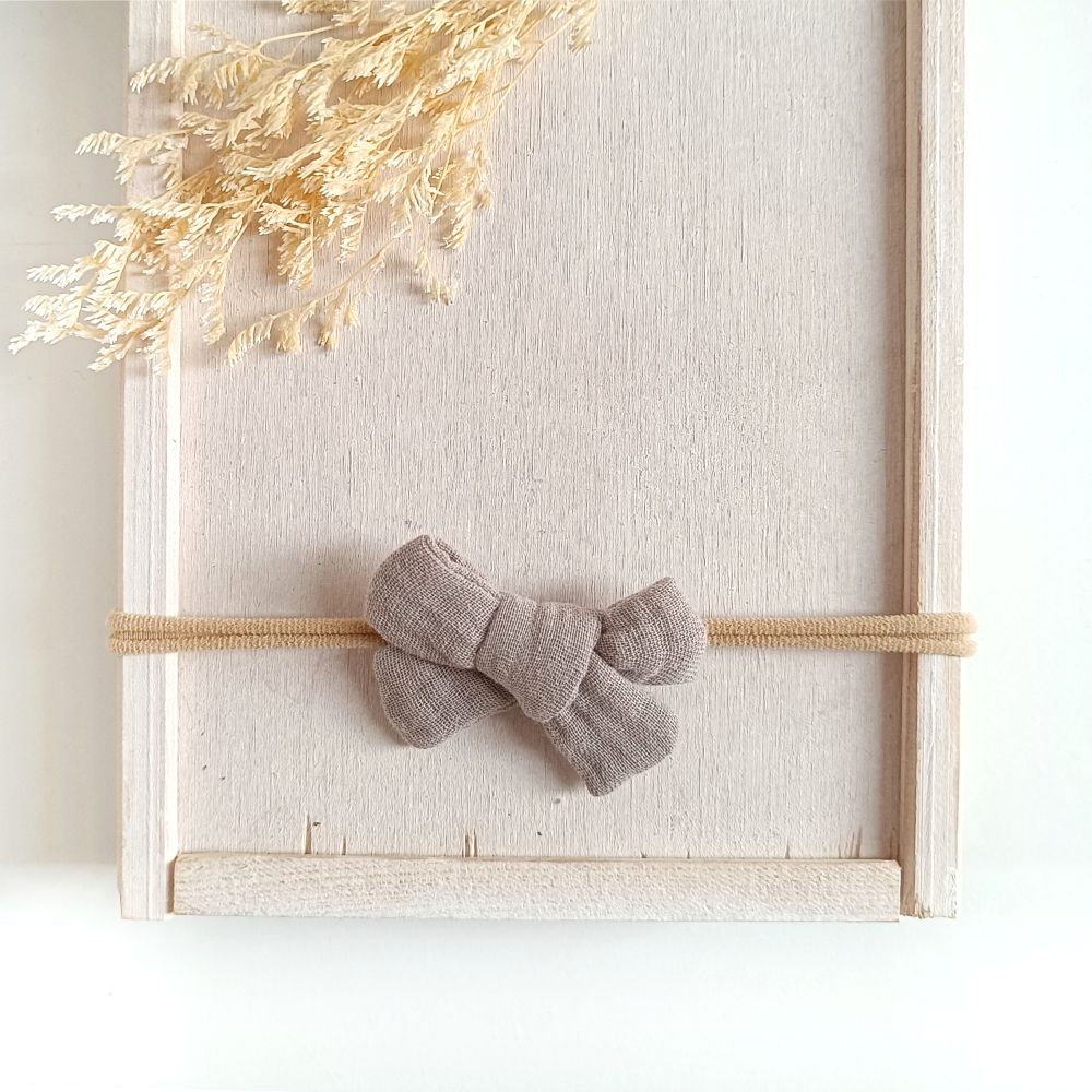 kleine Haarschleife aus Musselin für Babys in der Farbe taupe an einem elastischen Haarband