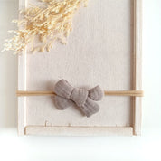 kleine Haarschleife aus Musselin für Babys in der Farbe taupe an einem elastischen Haarband