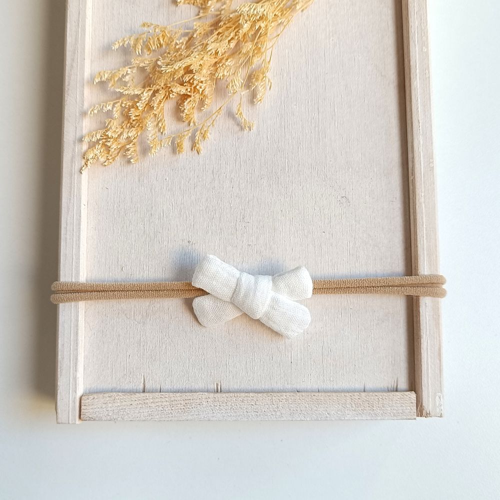 kleine weiße Haarschleife für Babys aus Musselin an einem elastischen Haarband